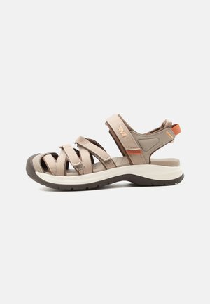 Beige udendørs sandal med justerbare remme, polstret sål, lukket tåbeskyttelse og orange hælstræk, vist fra siden.