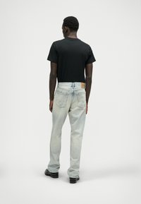 Jeans de denim azul claro com um corte descontraído e uma textura ligeiramente desgastada, combinados com uma t-shirt preta de mangas curtas. Sapatos pretos básicos.