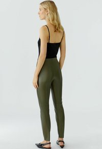 Zwarte cami met dunne bandjes, gecombineerd met strakke olijfgroene leggings. De leggings hebben een gladde textuur en een smalle snit. Zwarte ballerina's.