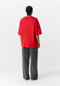 Rød bomulds t-shirt med korte ærmer, afslappet pasform og rund udskæring, parret med højtsiddende, bredbenede grå bukser.