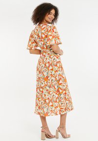 Vestido de estampado floral con mangas cortas acampanadas, base naranja y acentos en tonos pastel. Tela fluida con cintura ceñida y bajo a media longitud.