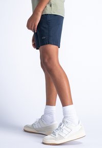 Marineblauwe shorts met een standaard pasvorm en gestikte zoom, gecombineerd met witte sneakers met een suède en mesh ontwerp, gedragen met witte sokken.