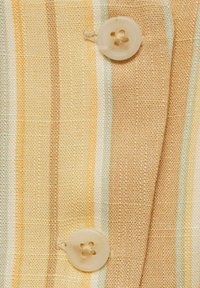 Striped fabric in yellow, cream, and orange tones, featuring a translucent button with four holes, highlighting a textured weave.