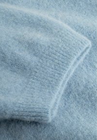 Hellblauer, flauschiger Strickstoff mit eingefaltetem Bündchen, der die weiche Textur und feinen Fasern aus der Nähe zeigt.