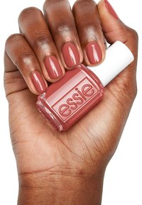 Essie nagellakflesje vastgehouden in een hand. De lak heeft een verzachtte rozenkleur, met glanzende nagels en een simpele witte dop en gegraveerd etiket.