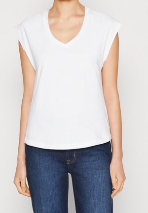 Biała bawełniana koszulka V-neck z krótkimi rękawami, prostym dołem i miękką fakturą. Połączona z ciemnoniebieskimi dżinsami dla kontrastu.