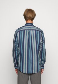 Prugasta srajca v odtenkih modre, turkizne in sive. Ima dolge rokave, gumbaste manšete in klasičen ovratnik s zaobljenim robom.