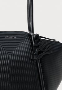 Svart texturerad läderhandväska från Karl Lagerfeld med geometriska mönster, dubbla remmar och en svart signaturberlock knuten nära dragkedjan.