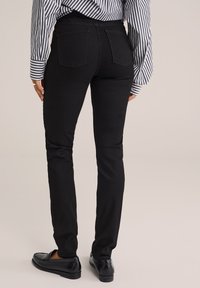 Čierne denimové nohavice so slim fit strihom, stredným pásom a dvoma zadnými vreckami, kombinované s čiernymi mokasínami a pásikavou košeľou.