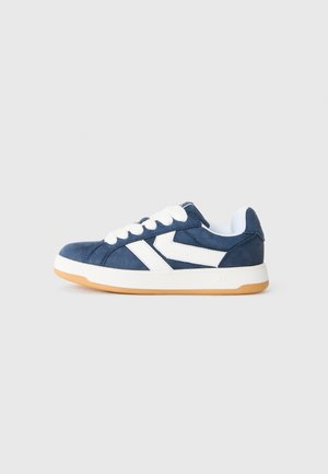 Baskets en suede bleu marine avec des accents en chevron blancs, des lacets blancs, un collier rembourré et une semelle en caoutchouc beige, présentées de côté sur un fond uni.