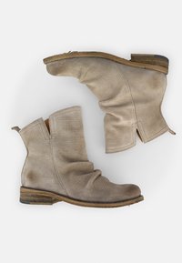 Botas de tobillo de cuero perforado beige con un diseño arrugado, tacón de madera bajo y punta redonda. Presentan una apertura lateral y tiradores en forma de bucle.