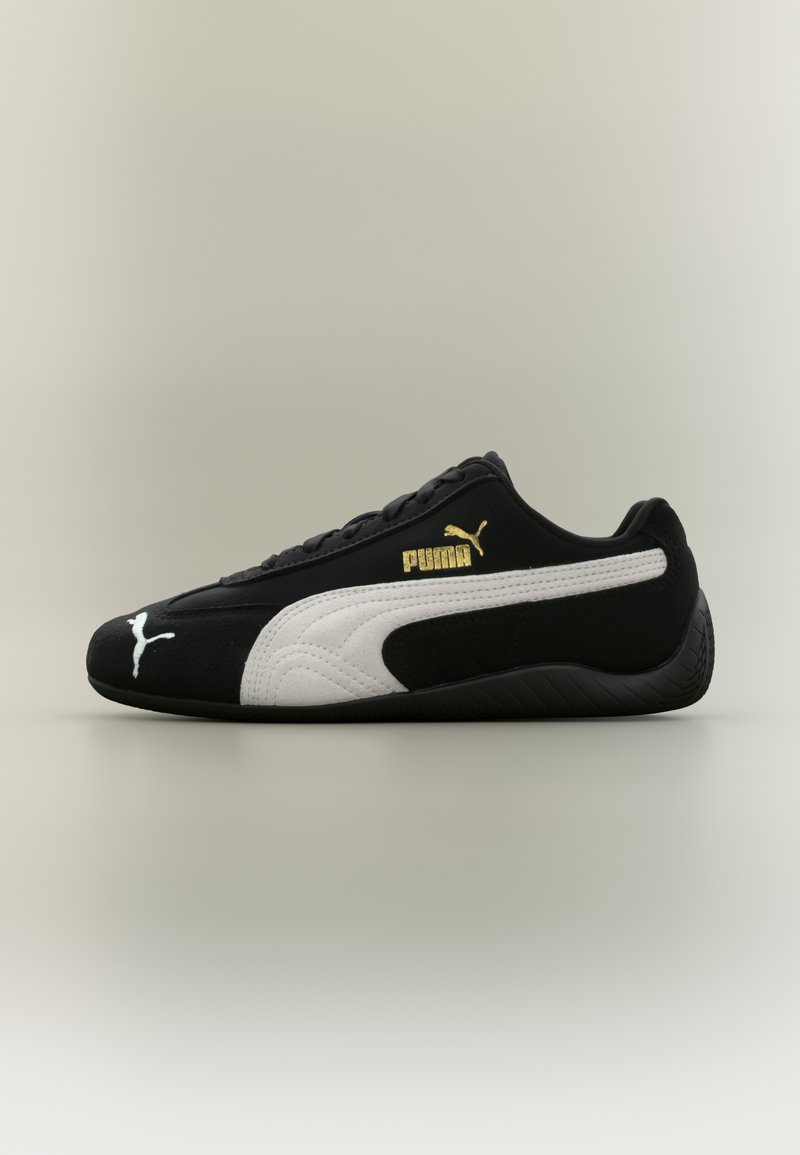 Schwarzer Sportschuh mit weißem Puma-Streifen und goldenem Puma-Logo an der Seite, von der Außenseite auf neutralem Hintergrund gesehen.