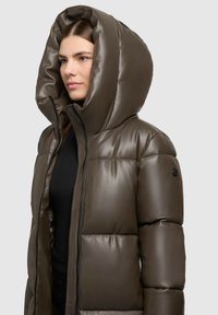 Jachetă puf de culoare maro, cu o glugă mare, pliată, închidere cu fermoar și un finisaj lucios. Prezintă un model texturat pe material și un detaliu cu logo.