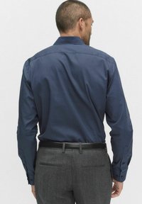 Granatowa koszula z długim rękawem w kropki, z kołnierzykiem rozłożystym, z mankietami zapinanymi na guziki. Nosi się z szarymi spodniami i czarnym paskiem. Gładka tekstura.