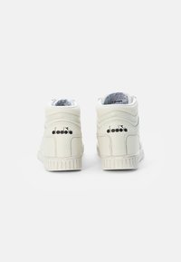 High-top sneakers in white leather with textured accents. Features a ridged rubber sole and black logo on the heel. Plain design, minimal detailing.