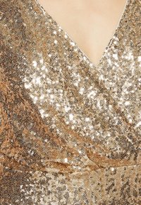 Gros plan d'une robe recouverte de sequins dorés avec un décolleté en V reflétant la lumière sur un fond de peau lisse.