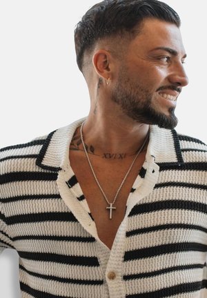 Schwarz-weiß gestreifter Strickcardigan mit Kragen, Holzknopf und tiefem V-Ausschnitt. Gestapelte Kettenhalsketten, eine mit einem Kreuzanhänger.