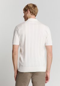 Witte korte mouwen polo met geribbelde textuur en verticale streepjespatroon. Bevat een klassieke kraag en een getailleerde pasvorm.