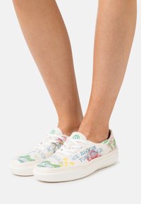Baskets en toile avec motifs floraux et graphiques multicolores, lacets blancs, accents verts et semelle texturée.