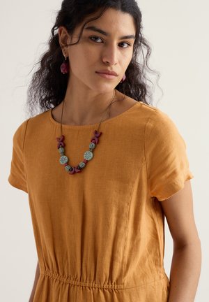 Mustársárga vászonruha rövid ujjakkal, rugalmas derékpánttal, sokszínű gyöngy nyaklánccal, amely kör alakú díszítéseket tartalmaz.