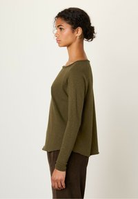 Olive green long-sleeve top with a round neckline, relaxed fit, and slightly frayed hem. Paired with brown corduroy pants.