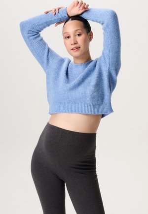 Himmelblauer, verkürzter Pullover mit gerippter Textur und langen Ärmeln, kombiniert mit hochgeschnittenen, dunkelgrauen Leggings. Einfaches, lässiges Design.