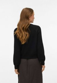 Melns džemperis ar mīkstu faktūru, apaļu kakla izgriezumu un pūkainām garām piedurknēm. Mugurpusē redzams piegulošs dizains, kombinēts ar svītrainu svārku.