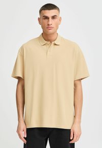 Beige polo skjorte med klassisk krage, korte ermer og en avslappet passform. Laget av teksturert stoff med en subtil glans.
