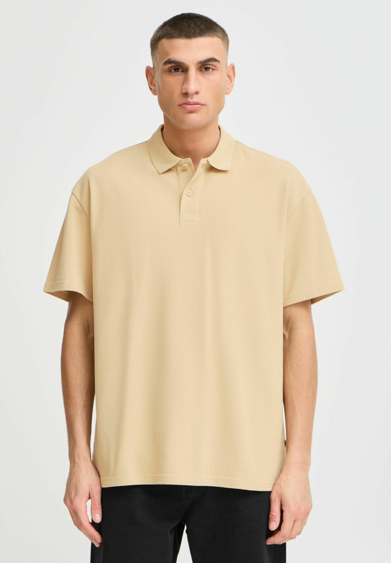 Beige polo skjorte med klassisk krage, korte ermer og en avslappet passform. Laget av teksturert stoff med en subtil glans.