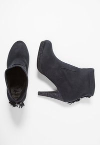 Botines de ante negro con tacón de aguja. Presentan un detalle brillante en el tacón y un forro suave. Puntera redonda y detalle decorativo de borlas.
