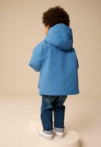 Blauwe hoodie met een gladde afwerking, gecombineerd met opgerolde blauwe spijkerbroeken en witte sneakers met rode accenten.