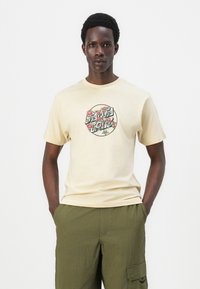 Beige cotton t-shirt featuring a circular graphic with red roses and text. Short sleeves, round neck, and relaxed fit. Paired with olive green pants.