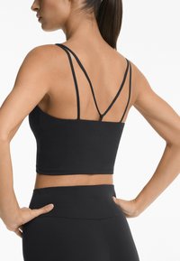 Black cropped tank top with thin cross-back straps. Made of smooth, stretchy fabric. Features a subtle brand logo at the back.