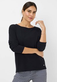 Zwarte lange mouwen top met een bootnek, relaxte pasvorm, geribbelde manchetten en een subtiele logo-accent aan de zoom, gecombineerd met een gedrukt broek.