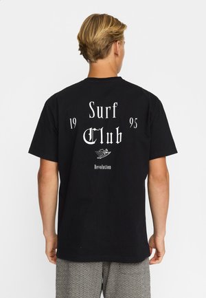 Maglietta nera in cotone con testo bianco: "Surf Club 1995" e un design grafico di una tavola da surf e onde, con una vestibilità ampia.