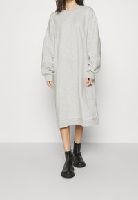 Vestido sudadera de gran tamaño en gris claro con mangas largas, puños acanalados y dobladillo recto. Combinado con botas negras hasta el tobillo.