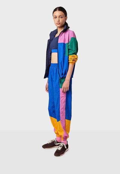 Kleurrijke windbreaker set met een marineblauw, roze, groen, blauw en geel color-block ontwerp. Bevat een cropped jack en broek met elastische tailleband.