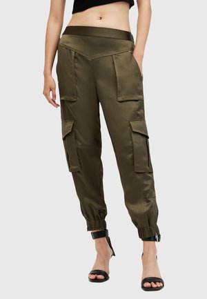 Kvinde iført olivengrønne cargobukser med flere lommer og elastiske manchetter, kombineret med sorte højhælede sandaler.