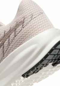 Ingrandimento di un tallone di una scarpa da corsa in rete beige con suola in schiuma bianca e suola nera testurizzata per grip.