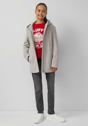 Grauer Reißverschlussmantel mit Kapuze, über einem roten Grafik-T-Shirt getragen. Schwarze Jeans und weiße Sneakers runden das Outfit ab. Glatte Textur.