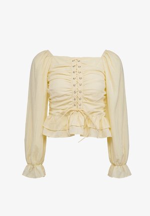 Blouse jaune clair à manches longues avec manches bouffantes, devant froncé, détail lacé et ourlet volanté aux poignets et à la taille.