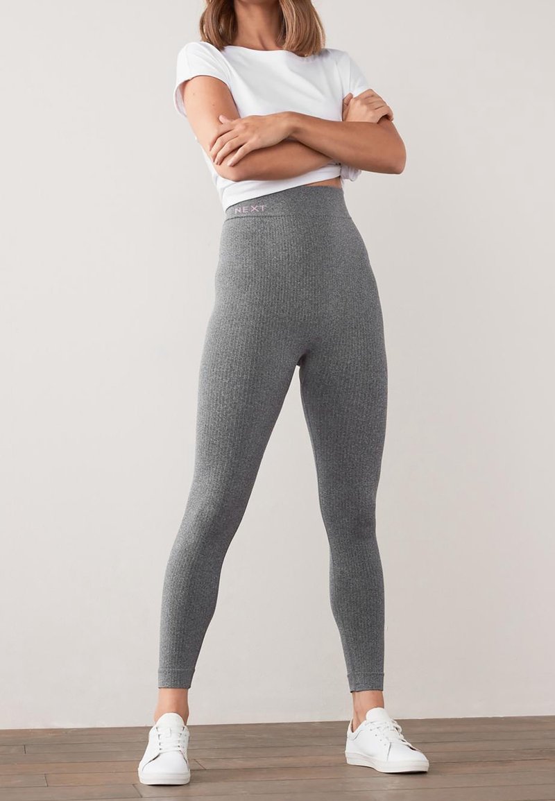 Leggings gris taille haute avec une texture côtelée, ornés d'une bande logo « NEXT » rose en haut, associés à des baskets blanches.