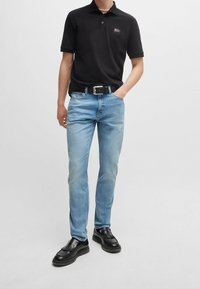 Svart pikétröja med en liten logotyp, ljusblå jeans, svart bälte och moderna svarta skor med fransdetaljer. Enkelt och funktionellt design.