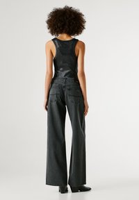 Melnā, pieguļošā topa no teksturētas auduma, savienota ar platām, tumši pelēkām džinsu biksēm ar aizmugurējiem kabatām un taisnu piegriezumu, valkāta ar melnām augstpapēžu kurpēm.