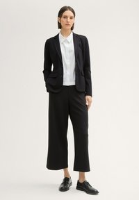 Black blazer with two buttons over a white collared shirt, paired with wide-leg black trousers and black lace-up shoes. Smooth fabric with subtle texture.