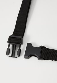 Schwarzer Nylonriemen mit zwei Kunststoffschnallen. Strukturiertes Material; verstellbares Design. Verfügt über einen Ver- und Entriegelungsmechanismus für eine sichere Befestigung.