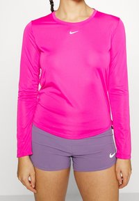 Langsleeve sporttop in felroze, gemaakt van gladde, rekbare stof. Heeft een ronde hals en een klein wit Nike-logo op de borst.