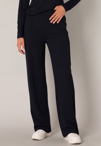 Marineblauwe wijde pantalon gemaakt van zachte stof, met een soepele tailleband en een ontspannen pasvorm, gecombineerd met witte sneakers.
