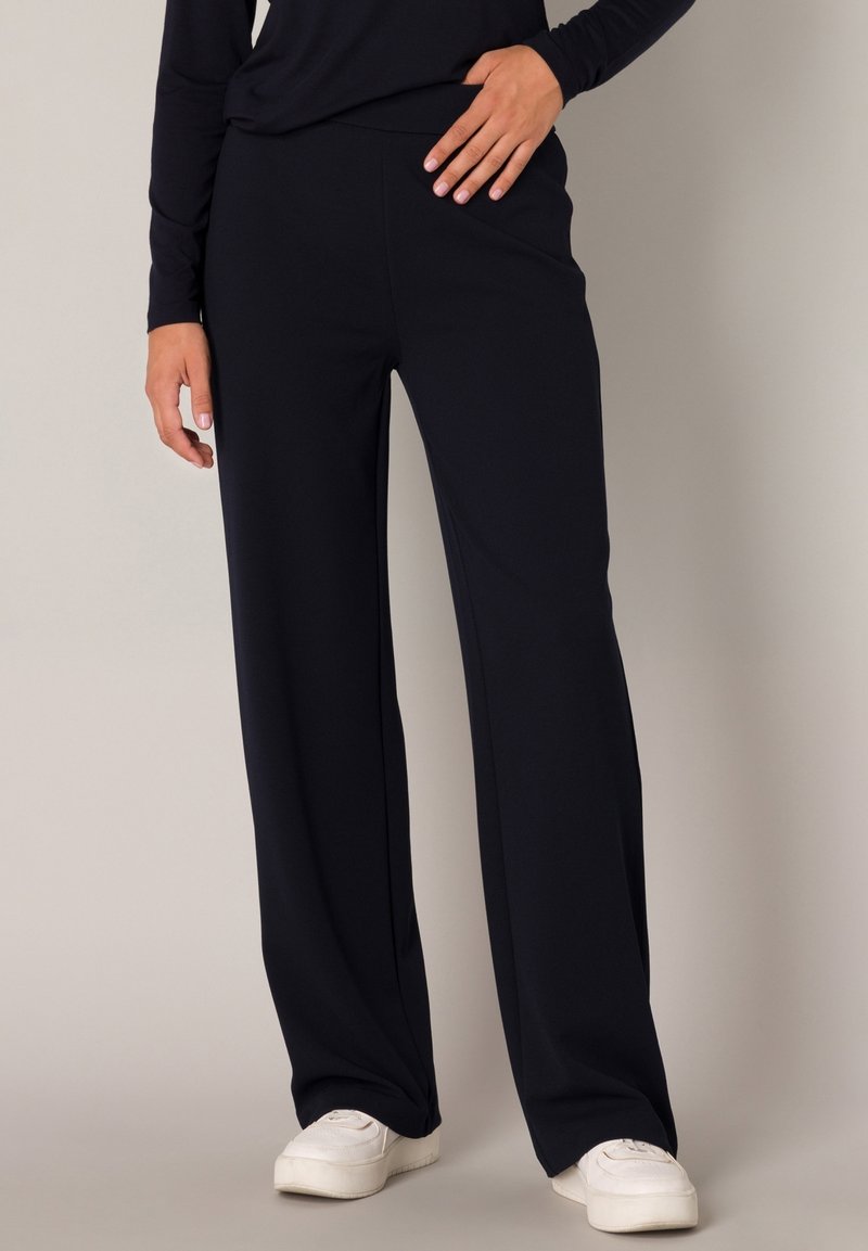 Marineblauwe wijde pantalon gemaakt van zachte stof, met een soepele tailleband en een ontspannen pasvorm, gecombineerd met witte sneakers.