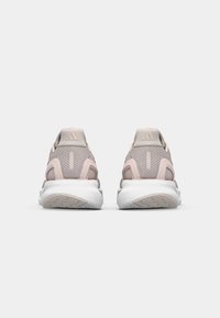 Baskets de sport rose clair avec une tige en mesh, un col rembourré et une semelle intermédiaire blanche. Marquage notable à trois bandes à l'arrière.